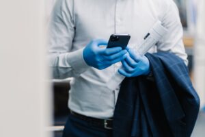 Businessman in elegant clothes types message on modern smartphone, wears protective gloves