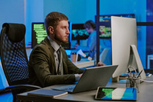 Young Caucasian male programmer working on computers at workplace in cybersecurity office, medium shot