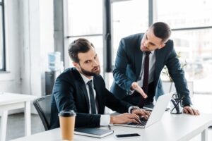 Selective focus of dissatisfied businessman typing on laptop near emotional man in formal
